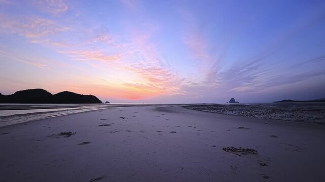 Curving tidal flats leading toward distant offshore rock at pastel twilight in Thailand