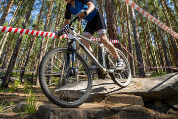 Fototapeta premium Mountain biker ride on large stones in forest fenced with marking tape