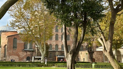 Ancient Church of Saint Irene (Hagia Irene) in Istanbul, Turkey. View through green trees in the outer courtyard of Topkapi Palace. Historic Byzantine architecture with red brick walls and arched wind