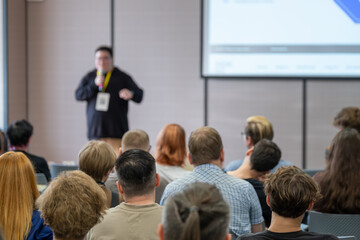 Lecturer presents to attentive audience in conference room with screen projection.