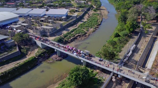 Aerial view of Dominican&ndash;Haitian border in Dajab&oacute;n as crowds gather on bridge for market day. Traders, vehicles and colorful umbrellas fill crossing during preparations for cross-border commerce.