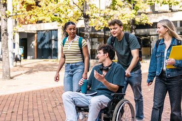 Fototapeta premium College students with a friend in a wheelchair chatting while walking on an inclusive university campus. Friendship and education concepts