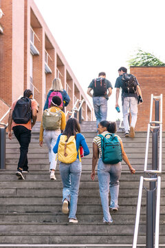 Diverse group of university students walking up exterior stairs, carrying backpacks, at a modern campus building