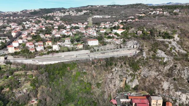 Drone aerial footage over the Rijeka bypass highway featuring viaduct, tunnel and hilly landscape near Rijeka, Croatia. Transport infrastructure, sunny day