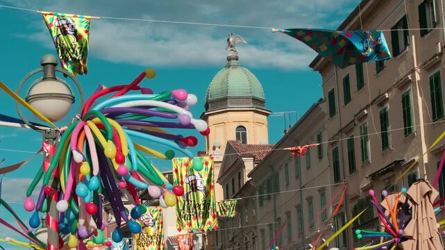 Slow motion close-up of colorful balloons hanging above a historic street in Rijeka. Old town architecture in the background creates a festive carnival atmosphere on a sunny day.