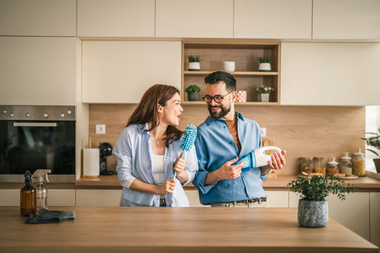 Couple dancing and singing while house cleaning in kitchen