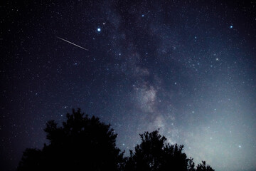 Fototapeta premium Milky way stars and constellations with landscape silhouettes photographed from a dark countryside location.