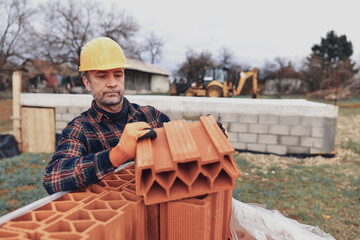 Bricklayer mason holding a regular brick outdoors on a construction site.