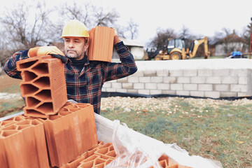 Bricklayer mason holding a regular brick outdoors on a construction site.