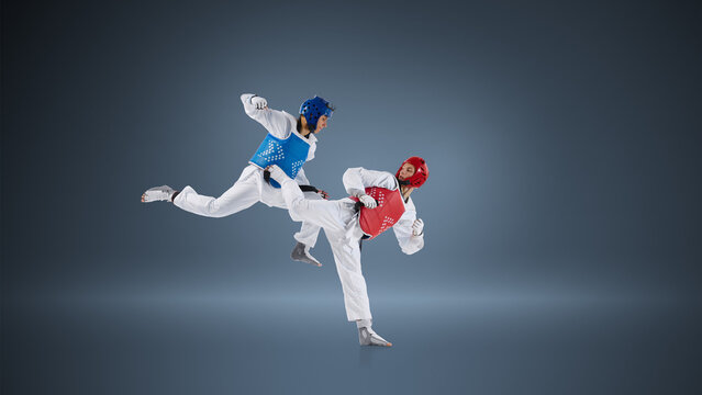 Professional taekwondo fighters in dynamic kick exchange on blue background wearing protective helmets and chest guards. Concept of elite combat sport, competitive sparring and athletic performance.