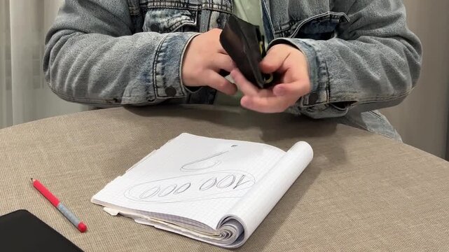 Video close up. 60 fps. Man in blue jeans denim jacket at table counts cash money in hotel living room. Text 100000 in notebook. Paper banknote - dram. Concept of pay debt, budget, loan, salary, tax