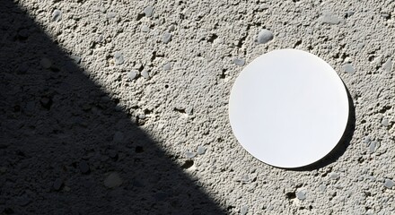 A white circular object casting a shadow on a textured concrete surface.