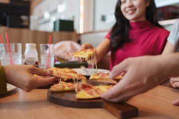 Friends sharing delicious pizza with stretching cheese at restaurant