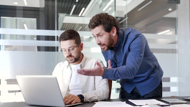 Angry manager quarreling with upset subordinate while sitting at laptop at workplace in business office. Furious boss arguing talking about problems. Dissatisfied executive unhappy with work results