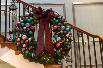 large festive wreath with colorful baubles hanging on a grand staircase.