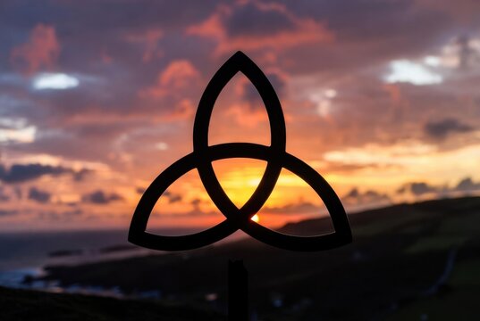 Celtic trinity knot silhouette against a vibrant sunset landscape symbolizing irish heritage and tradition.