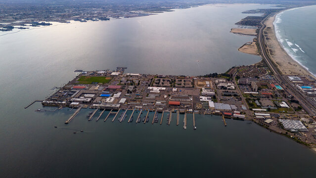 Aerial view of the sprawling naval base, a tapestry of gray buildings and piers jutting into the dark water, reflecting the overcast sky, Coronado, California, United States.