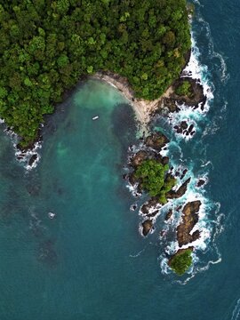Aerial view of a lush, green headland embraced by the turquoise sea, where jagged rocks meet the sandy shore, Mutis, Choco, Colombia.