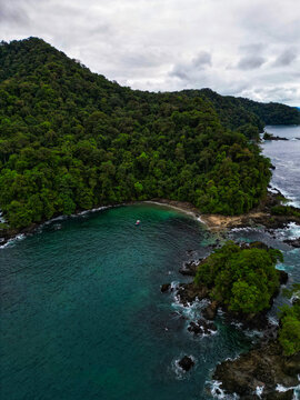 Aerial view of the vibrant turquoise water gently kissing the dark, rocky shorelines, and lush green forest covering the land, Mutis, Choco, Colombia.