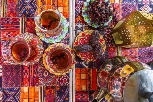 Three glasses of tea served with dates on patterned oriental carpet. Traditional Middle Eastern hospitality concept, Ramadan iftar atmosphere.