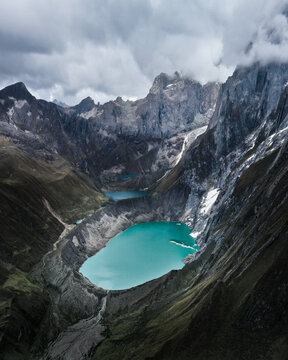 Aerial view of the turquoise waters of Laguna Paron nestled amidst the rugged peaks of the Cordillera Blanca, a stunning contrast of color and texture under a cloudy sky, Caraz, Ancash, Peru.