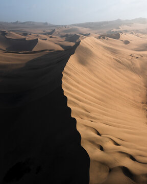 Aerial view of the sun-kissed dunes casting deep shadows across the desert landscape, creating a mesmerizing contrast of light and shade, Ica, Ica, Peru.