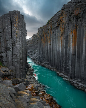 Aerial view of the striking basalt columns rise majestically above the turquoise river, a solitary figure stands in awe of the natural grandeur, Eiriksstadhir, Mulathing, Iceland.