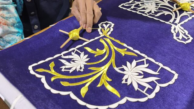 A skilled artisan performs traditional Malay Tekat embroidery. He meticulously sews gold thread onto rich velvet fabric. This rare, ancient craft represents a vanishing heritage art form.