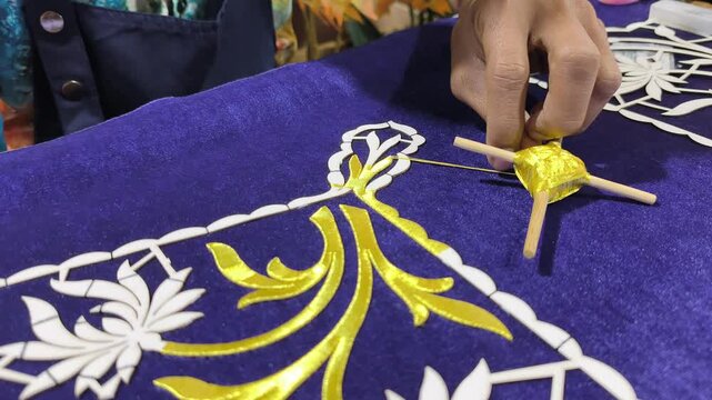A skilled artisan performs traditional Malay Tekat embroidery. He meticulously sews gold thread onto rich velvet fabric. This rare, ancient craft represents a vanishing heritage art form.