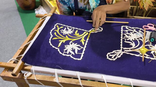 A skilled artisan performs traditional Malay Tekat embroidery. He meticulously sews gold thread onto rich velvet fabric. This rare, ancient craft represents a vanishing heritage art form.
