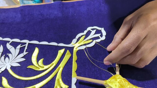 A skilled artisan performs traditional Malay Tekat embroidery. He meticulously sews gold thread onto rich velvet fabric. This rare, ancient craft represents a vanishing heritage art form.