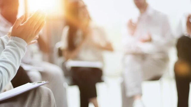 A hand writes with a pen in a notebook against the background of colleagues sitting on a chair