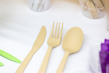 Beige plastic knife, fork, and spoon neatly arranged on a white surface, photographed in close-up, representing sustainable disposable utensils
