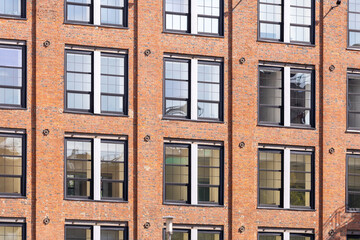 Historic red brick industrial building with large windows in an urban environment. Industrial style architecture with modern renovations under a clear sky