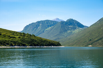Majestic mountain landscape under clear blue sky featuring calm lake and lush green slopes, showcasing the beauty of nature in summer, reflecting tranquility and serenity