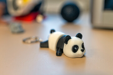 Panda keychain figure resting on a table with various items in the background © ako-photography