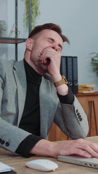 Bored sleepy business man worker working on laptop computer, yawning, leaning on hand falling asleep at office workplace. Exhausted tired freelancer workaholic man. Employment, occupation, workless
