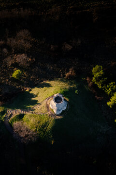 Aerial view of a medieval tower atop a grassy hill, encircled by shadows and the forest's dark embrace, Nin, Zadar County, Croatia.