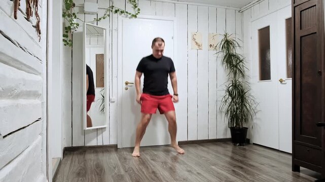 A man jumps up and crosses his legs. A person practices a Cris cross movement from a breakdancing lesson at home. Dancing hobby. Athletic human. Sports warm-up. Hot warmuping. High quality 4K footage.