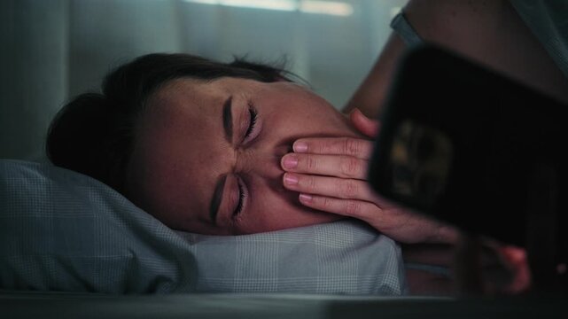 Tired Woman Yawns While Using Smartphone in Bed at Night