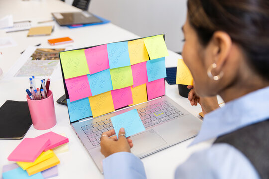 Manager organizing colorful sticky notes on computer in office workspace