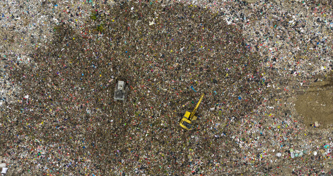 Aerial view of a vast landfill where a yellow excavator and a truck stand still among the sea of colorful refuse, Denpasar, Bali, Indonesia.