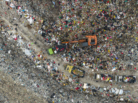 Aerial view of a vast, textured landscape of discarded waste, interrupted by heavy machinery and vehicles, creating a stark contrast, Denpasar, Bali, Indonesia.