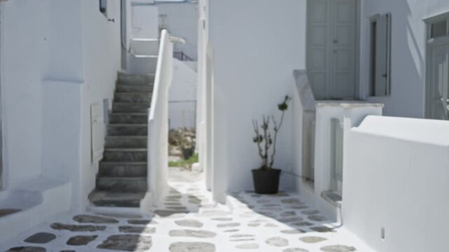 Mykonos whitewashed alley with stone paving and exterior stairs in soft defocused bokeh background street; background copyspace backplate.