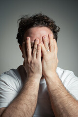 Man with Curly Hair and Beard Covering His Entire Face with Both Hands