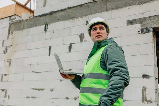 Construction inspector in hard hat and vest using laptop at building site