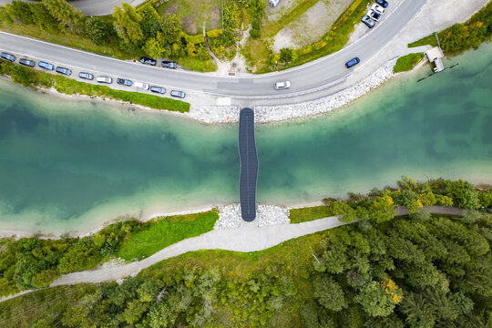 Aerial view of a bridge crossing a vibrant turquoise river, bordered by lush greenery and a winding road, Plansee, Tyrol, Austria.