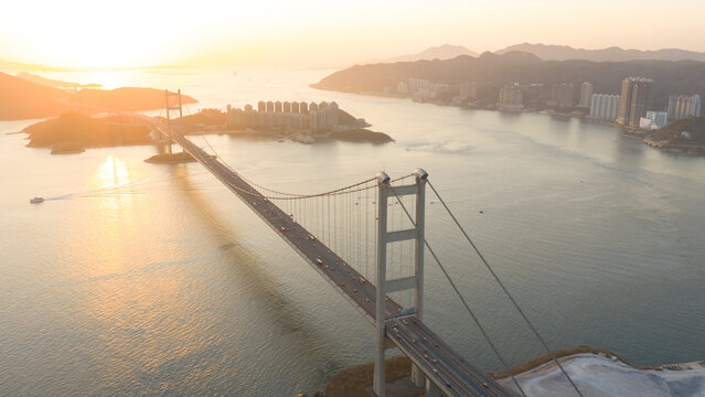 Aerial view of the magnificent Tsing Ma Bridge stretching across the tranquil waters to distant buildings under a golden sunset, Hong Kong, Hong Kong.