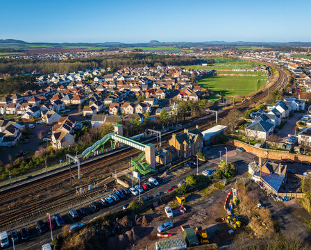 Aerial view of the Dunbar train station and its connecting footbridge, nestled between rows of houses and a sprawling green field, Dunbar, Scotland, United Kingdom.