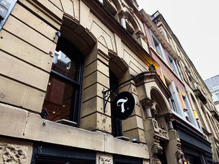 Naklejka premium Historic Manchester building on a street with arched windows and a round black T sign